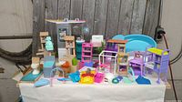 Overview of assorted Barbie dollhouse furniture and accessories arranged on table