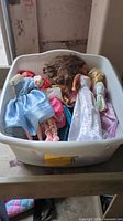 Plastic bin containing assorted fashion dolls in various outfits