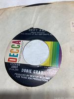 Photo of Dobie Gray 45 RPM vinyl record label "Drift Away" with DECCA rainbow label and original paper sleeve with wear.