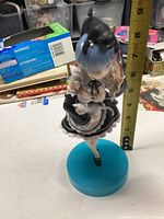 Front view of an anime figurine of a blue-haired girl in a black maid outfit holding a black kitten, viewed next to a tape measure showing the height of about 7.5 inches.