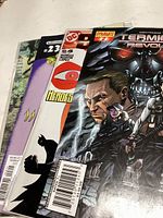 Photo showing four comic books fanned out, visible titles include Terminator Revolution and DC Heroes. Covers show various illustrated characters.