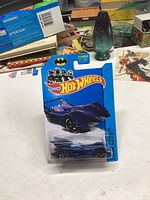 Photo of unopened 2013 Hot Wheels Batmobile die-cast car in original packaging with background items visible.