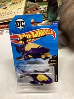Unopened Hot Wheels 2018 DC Batman Batcopter die-cast car in original packaging, showing the purple and yellow copter vehicle with black rotors and branding details.