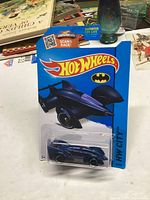 Photo of unopened Hot Wheels 2013 Batmobile diecast car in original packaging on table with other items in background.