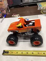 Photo of a large orange El Toro Loco monster truck toy with yellow horns and big black tires with orange rims, placed on a table next to a ruler for size reference of about 8 inches long.