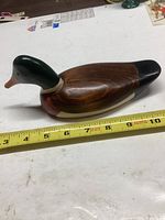 Side view of wooden mallard duck decoy showing painted head and body detail with measuring tape indicating length around 10 inches.