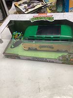 Front view of TMNT Leonardo figure beside green and beige 1962 Volkswagen bus in original TMNT branded packaging