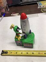 Side view of Pez dispenser with Marvin the Martian sitting beside silver rocket ship with red nose cone, showing height roughly 6 inches.