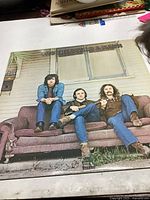 Front cover of Crosby, Stills & Nash vinyl record showing band members sitting on a brown couch in front of a porch.