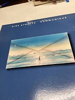Front cover of Dire Straits Communiqué album showing the artwork of a person walking on a beach with a sky backdrop.