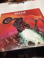 Front cover of Meat Loaf 'Bat Out of Hell' vinyl record album showing detailed artwork of a man on a motorcycle in a dramatic fiery background.