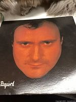 Front cover of vinyl record album depicting a large close-up image of Phil Collins' face with "Required" text in bottom left corner.
