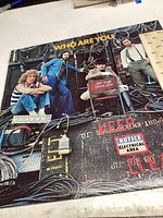 Front cover of the Who album 'Who Are You' featuring the band members sitting on stage equipment with signage.
