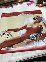 Front cover of the Rolling Stones 'Made in the Shade' vinyl record showing the woman in a red swimsuit lying down with sunglasses and headphones.