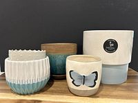 Group photo showing five ceramic plant pots in various styles and sizes, including the large white/light blue handcrafted pot, the medium two-tone pot, the small butterfly decorated pot, and the dotted textured small pot wedged inside the larger one.