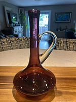 Front view of Bischoff amethyst glass decanter showing wide rounded base, tall neck, and clear handle on side. No stopper present.