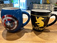 Front view of Captain America and Hufflepuff mugs side by side on a wooden surface