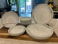 Set of Corelle dinnerware items arranged on countertop including dinner plates, side plates, soup bowls and serving bowl.