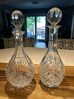 Pair of crystal decanters, Godinger Dublin on left with oval stopper, unbranded on right with ball stopper, displaying intricate cut patterns.