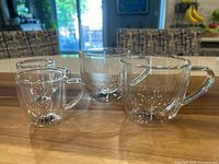 Four clear double wall glass cups on a wooden board, two larger cups for coffee/cappuccino and two smaller cups for espresso, shown together on a wooden surface.