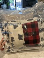 Bedding set in plastic packaging showing bear motif sheets and plaid fabric inside the bag