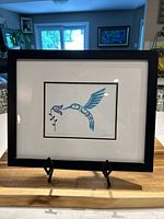 Framed art print displayed on a wooden surface with kitchen background.