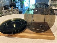 Set of six glass charger plates displayed on a wooden surface, showing the colors and etched acorn pattern.
