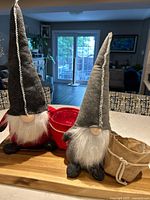 Two plush gnome planters placed on a wooden surface with red and beige Santa-style bags, showing overall size and details of hag and beards.