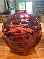 Front-side angle view showing the round form and vibrant pink color with violet swirling patterns.