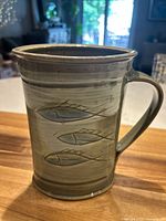 Front view of the green stoneware pitcher showing three embossed fish designs on the side and the handle.