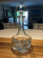 Full view of the tall clear lead crystal decanter with flat-top stopper on wooden surface, reflecting light.
