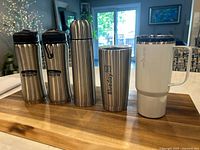 Five stainless steel bottles and cups arranged on wooden surface, showing all items front-facing