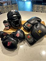 Pro Force helmet, MDSS fingerless gloves, Budo World boxing gloves, and two Top Ten wraps displayed on table.