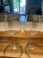Pair of clear glass musical wine glasses on wooden surface with musical note scale lines from A to G marked on the bowls.