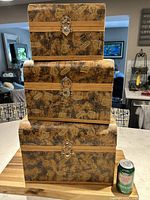 Three nesting chests stacked on top of each other with a soda can nearby for size reference. The chests have a brown and tan leather-like patterned exterior with snap closures.