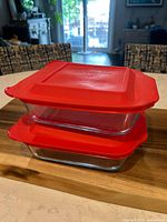Stacked view of the two clear glass Pyrex baking dishes with red lids on a wooden surface.