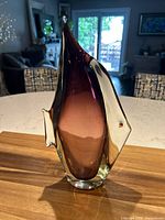 Front view of sommerso-style art glass fish sculpture showing clear glass with purple/maroon interior and red eyes on a wooden surface.