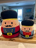 Front view of two Squishmallows nutcracker plush toys, one larger in red and one smaller in blue.