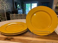 Four goldenrod yellow round dinner plates stacked and one displayed upright on a stand on a wooden surface in a home setting.