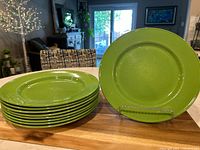 Nine stacked green steelite dinner plates with one plate displayed vertically on stand, showing smooth glossy finish and uniform color.