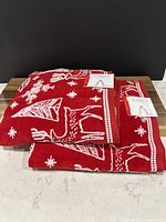Two folded red towels with white holiday motifs and visible Caro brand tags on top, showing new condition and pattern details.