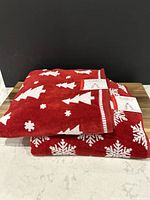 Two folded holiday towels stacked, red towel on top with white Christmas trees and snowflakes, tags visible.