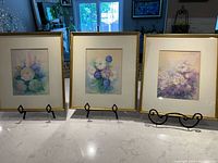 All three floral watercolours displayed on a surface with gold frames; easels included for display only.