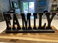 Front view of black wooden FAMILY sign with silver and rust accents on base on countertop in living room setting