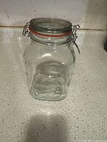 Full view of clear glass storage jar showing clamp metal top lid and orange rubber gasket on white countertop.