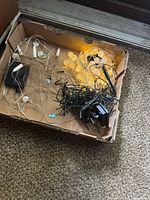 Two tangled sets of solar string lights, one black cord, one white cord, with solar panels and plugs inside a cardboard box.
