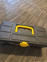 Closed black plastic toolbox with yellow handle and latch on wood floor