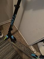 Side and deck view of the black Core kick scooter showing the textured deck and medium-sized wheels with blue and green accents.