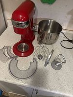 Red Cuisinart stand mixer with stainless steel bowl and multiple attachments displayed on countertop.
