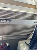 Front view of white Danby window AC unit showing horizontal vent grills and digital control panel with buttons and branding text, dusty and dirty exterior visible.